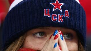 A close-up of a Russian sport fan. She has her nails painted Russia colours and looks on with worry.