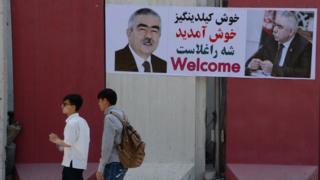 Afghan residents walk past a banner with the image of self-exiled Afghan Vice President Abdul Rashid Dostum