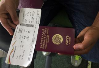 A passenger displays an Ethiopian passport and an Ethiopian Airlines boarding pass as he sits inside ET314 flight to Eritrea