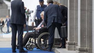 Jean-Claude Juncker is seen seated in a wheelchair as he is brought in through a side entrance of the building
