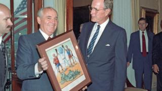 President of the USSR Mikhail Gorbachev presents US President George Bush (R) a friendly jest of a Soviet painter.
