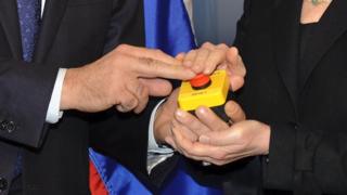 The hands of US Secretary of State Hillary Clinton and Russian Foreign Minister Sergei Lavrov rest on a red button marked 'reset' in English and 'overload' in Russian