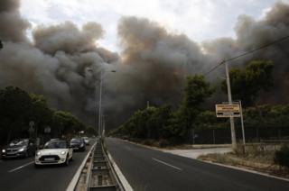 Smoke rises over a motorway in Neo Voutsa, a northeast suburb of Athens