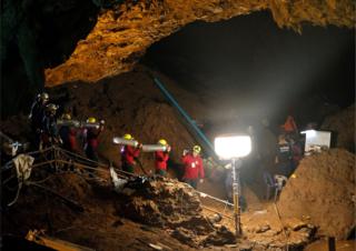 Thai officials carry oxygen tanks through a cave complex at the Tham Luang cave