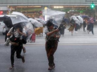 Umbrellas turns inside out as pedestrians struggle across a road in Tokyo