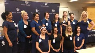 12 of the 16 pregnant nurses pose with their bumps on show in uniform