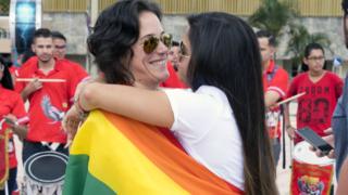 A female couple hug each other wrapped in a pride flag outside the Supreme Court