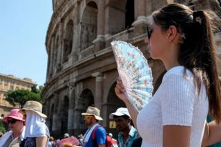 A tourist uses a fan during a hot Summer day in front of the Ancient Colosseum in central Rome