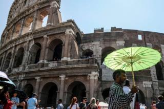 A man holds an umbrella to protect himself from the sun during a ho Summer day in front of the Ancient Colosseum in central Rome