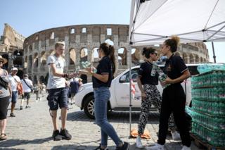Members of the Italian Civil Protection (Protezione Civile) distribute water bottles to people in front of the Ancient Colosseum, in central Rome