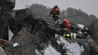 Rescuers climb by foot over large pieces of road wreckage, amid rain and poor conditions