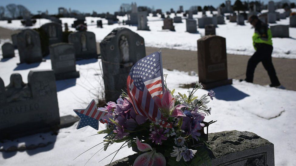 An American flag and flowers on a grave in Gloucester, Massachusetts