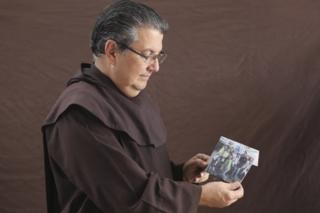 Father Cristóbal Domínguez holds up a photo of youth from hs parish