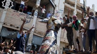 Rebels celebrate as they tear down 'hand crushing a plane' statue in Colonel Gaddafi's compound in Tripoli