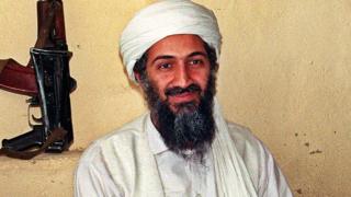Image of smiling Osama bin Laden with firearm in background