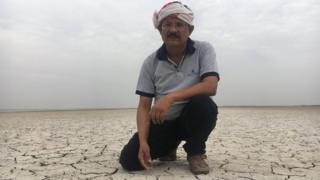Indian man in turban kneels down on cracked earth covered in a thick layer of white salt