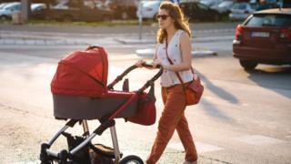 Woman crossing a road with a baby in the pram