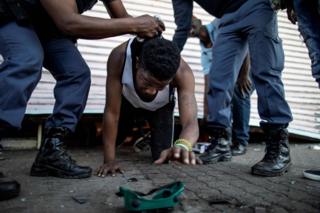 A suspected looter is detained by South African police officers as he emerges from of a looted foreign-owned shop in Soweto, Johannesburg