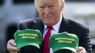 US President Donald Trump displays hats that read: 