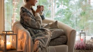 Stock image of woman wrapped up in knitwear with fairy lights and a hot drink