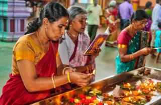 Tamil Hindu women light small lamps while offering prayers at a temple in Matale, Sri Lanka.