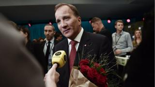 Swedish PM Stefan Lofven talks to the press, carrying red roses, after a TV debate on 7 September 2018