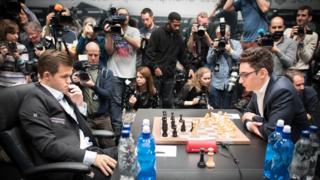 Magnus Carlsen (left) and challenger Fabiano Caruana face each other over a chess board while a host of photographers clamber in the background