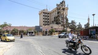 A man rides a motorcycle along a street past the damaged former Carlton Hotel building that serves as a Syrian Red Crescent hospital, in the rebel-held northern Syrian city of Idlib