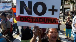 A Venezuelan opposition activist, holds a sign reading 